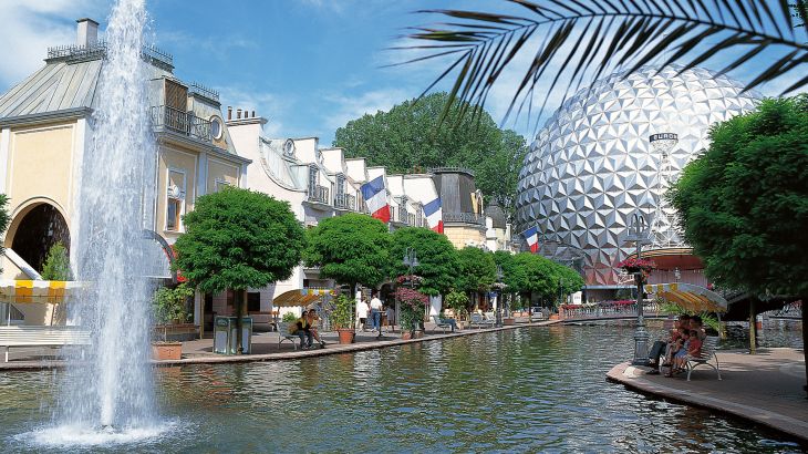De promenade van het Franse themagebied wordt omzoomd met waterfonteinen en veel groene bomen en loopt langs de gevels van Franse huizen.