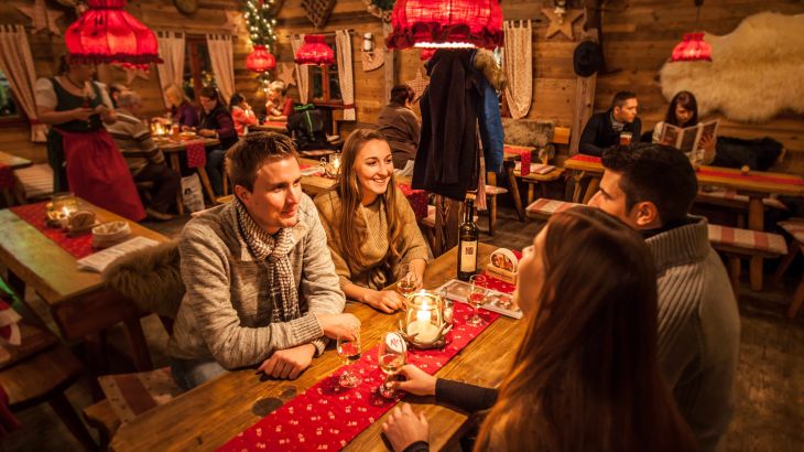 Piccoli gruppi siedono ai tavoli di legno nell’accogliente ERDINGER Hütt’n e trascorrono una serata conviviale.